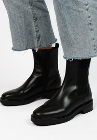 Zwarte leren enkellaarsjes met een gladde afwerking, elastische zijpanelen en een robuuste zwarte zool. Draagt met versleten lichtblauwe spijkerbroeken.