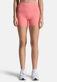 Shorts de sport roses à taille haute, fabriqués en tissu extensible, avec une texture lisse et une coupe ajustée, associés à des baskets blanches.
