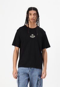 T-shirt nera a maniche corte con un design floreale bianco centrale, realizzata in cotone, con una vestibilità rilassata e scollo rotondo.