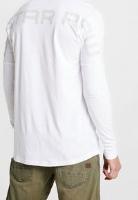 Vit långärmad skjorta med en diskret "STAR RAW" grafisk design på baksidan. Kombinerad med olivgröna cargobyxor med dubbla bakfickor.