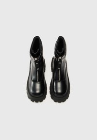 Bottines noires en cuir lisse avec une fermeture éclair, dotées d'une semelle en caoutchouc épaisse et de coutures audacieuses.