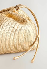 Gold woven fabric drawstring bag with a textured finish, featuring sleek gold hardware and smooth cord accents. Compact and soft shape.