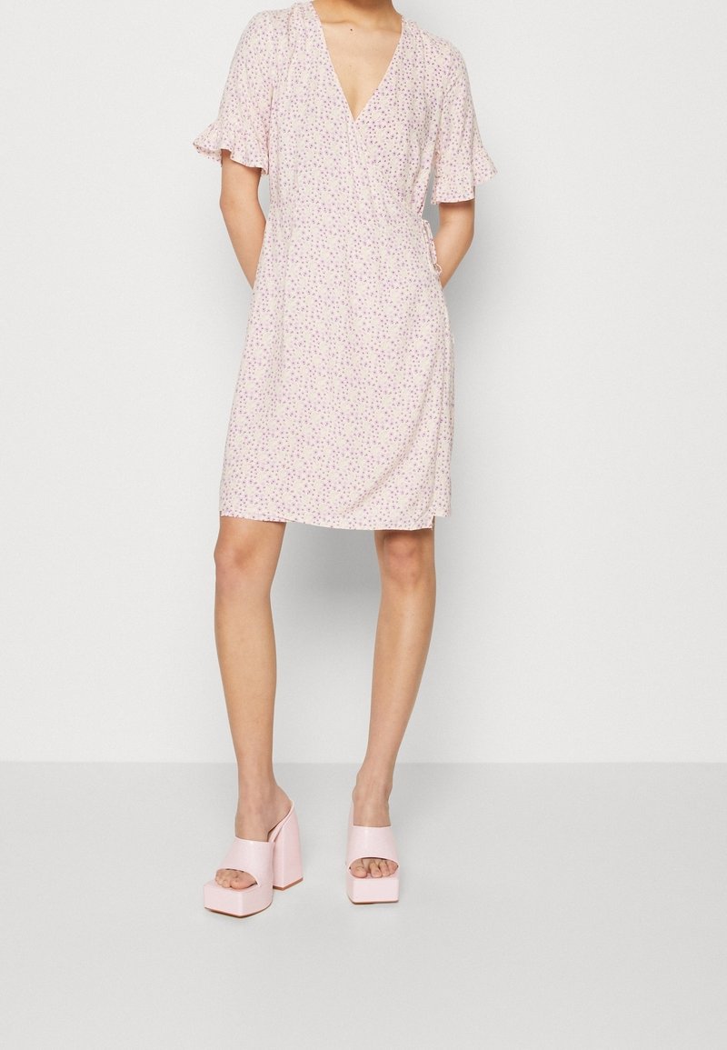 Floral-patterned, short-sleeve wrap dress in soft pink, featuring a deep V-neck and a relaxed fit, paired with chunky pink platform heels.