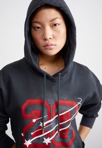 Black hoodie featuring a large red "28" graphic with white stars and swirls. Material appears soft, with a drawstring hood and relaxed fit.