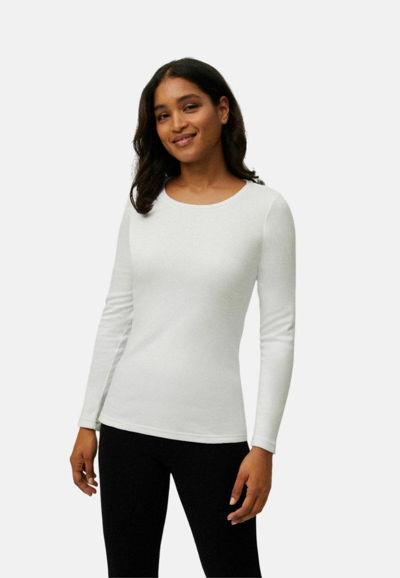 Top blanco de manga larga con escote redondo y textura suave, combinado con leggings negros. El ajuste es ceñido, resaltando la silueta.
