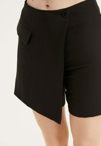 Zwarte op maat gemaakte shorts met een knoopsluiting, voorzien van een zijzak en een asymmetrisch zoomontwerp, gemaakt van een gladde stof.