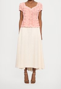 Haut à texture florale en rose pâle avec des manches courtes, associé à une jupe trapèze beige longueur genoux. Des sandales à talons beiges complètent la tenue.