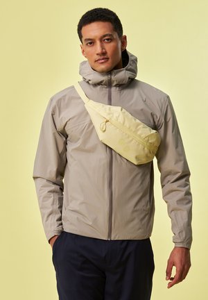 Lightweight beige jacket with a high collar and zipper; features a yellow crossbody bag with a smooth texture and circular accents.