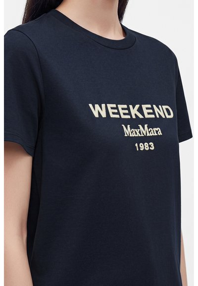 Femme portant un t-shirt bleu marine avec du texte crème "WEEKEND MaxMara 1983" sur le devant.