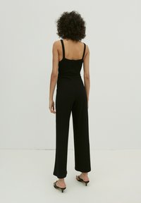 Jumpsuit negro acanalado con tirantes finos, corsé ajustado, piernas anchas y cierre de cremallera en la parte posterior. Llevado con sandalias de tacón.