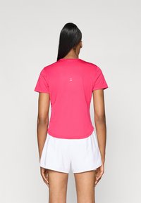 Tricou sportiv roz cu mâneci scurte, tiv rotunjit și un mic accent logo pe spate, asortat cu pantaloni scurți albi.