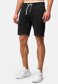 Pantalones cortos de algodón gris oscuro para hombre con cordón, dobladillo enrollado y bolsillos laterales, combinados con zapatillas blancas que cuentan con detalles de malla y cuero.