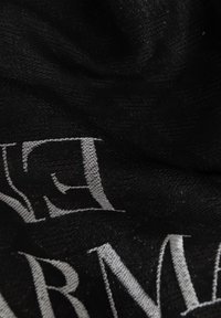 Tessuto nero con una superficie texturizzata, caratterizzato da lettere bianche parzialmente visibili, che suggeriscono un motivo o un dettaglio di marca.