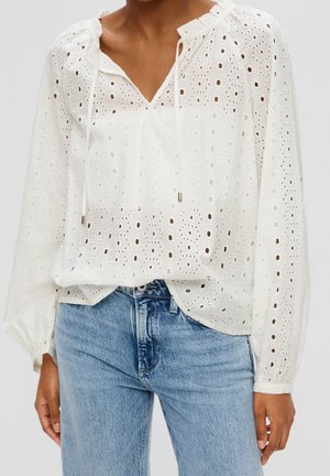 Blouse blanche à manches longues en œillet avec un col lacé associée à un jean taille haute bleu clair, portée par une personne à la peau de ton moyen.
