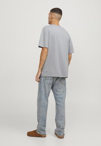 Grijze short-sleeve t-shirt met een ontspannen pasvorm, gecombineerd met lichtblauwe denim jeans. Het materiaal lijkt op katoen en heeft een soepele textuur.