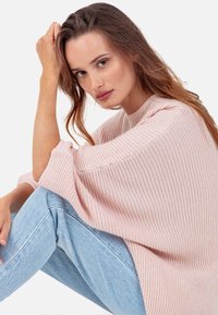 Pull rose pâle en maille côtelée avec une coupe ample et des manches larges, associé à un jean bleu clair. La texture est douce et accueillante.