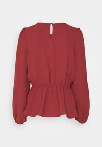 Blouse rouge à manches longues avec une silhouette peplum, en tissu texturé, et une ouverture en forme de trou de serrure avec boutons à l'arrière.