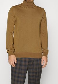 Bruine coltrui gemaakt van zachte stof, met lange mouwen en geribbelde manchetten, gecombineerd met een broek met een geruit patroon.