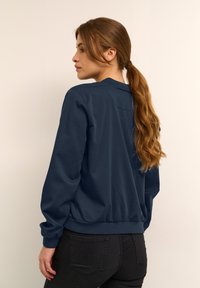 Sweatshirt bleu marine foncé avec un col rond et des épaules structurées. Comprend des poignets et un ourlet côtelés, un tissu texturé et une coupe décontractée.