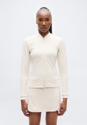 Helebeežitäpi värvi sportlik komplekt, mis sisaldab keha järgivat pika varrukaga topi luku sulgumisega ning sobivat seelikut küljetaskutega. Sile tekstuur.