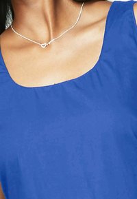 Blue sleeveless top with a rounded neckline; features smooth fabric texture. A silver chain necklace with a small heart pendant is visible.