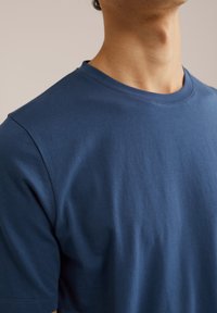 Mornarsko modra bombažna majica s krožnim ovratnikom, kratkimi rokavi in gladko teksturo. Ni opaznih vzorcev ali dodatnih detaljev.