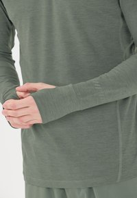 Langsleeve, olijfgroene top gemaakt van een zachte, lichte stof. Voorzien van duim gaten bij de manchetten en subtiele stikdetails langs de naden.