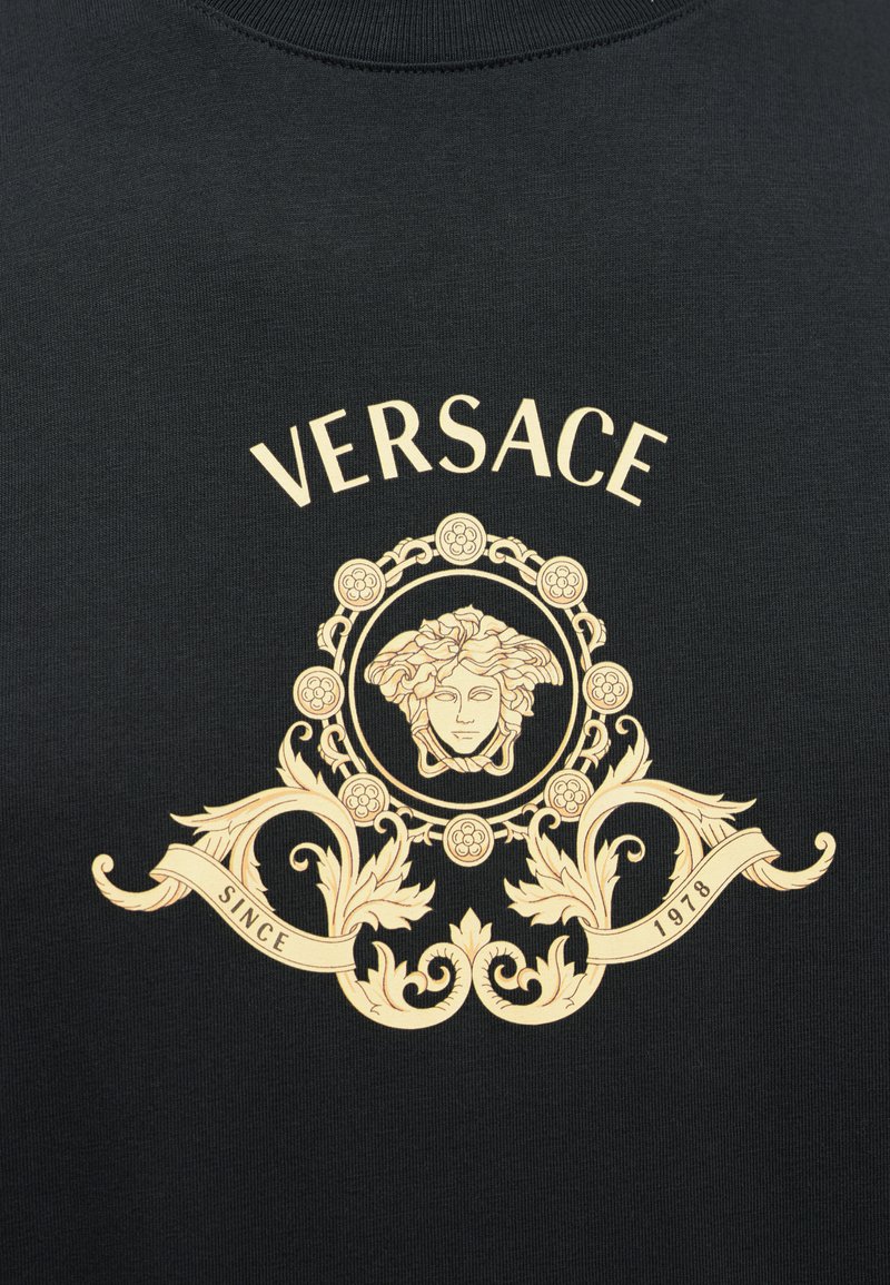 Sort bomuld T-shirt med et guld Versace-logo design med en central Medusa-motiver, udsmykkede blomsterdetaljer og et banner med teksten "SINCE 1978".
