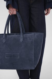 Laivastonsininen mokkanahkainen olkalaukku, jossa on kaksi kahvaa ja painettu logo edessä. Yhdistetty tummansinisiin farkkuihin.