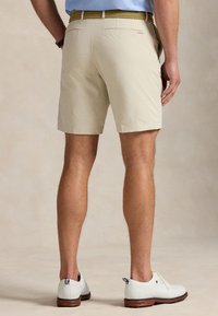 Pantalones cortos beige hechos de tela ligera, con un corte casual, bolsillos traseros y combinados con zapatos blancos.