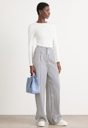 Witte lange mouwen top met klein logo, hoog-was gestreepte broek in blauw en wit, lichtblauwe handtas, en witte sneakers.
