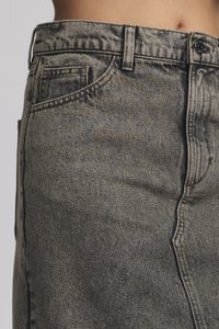 Szürke denim szoknya magas derékkal, vastag varrással, elülső zsebekkel és enyhe kopásmintával rendelkező textúrájú felülettel.