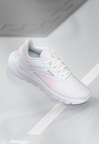 Chaussure de sport blanche avec des accents roses, un dessus en synthétique lisse et une semelle texturée. Les caractéristiques incluent des lacets et des détails de logo distincts.