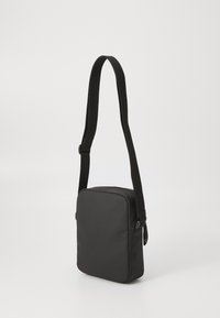 Black shoulder bag with a rectangular shape, made from smooth nylon, features an adjustable strap and a zip closure. No additional details visible.