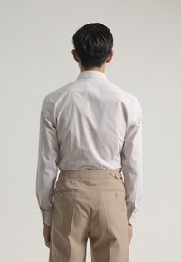 Camisa de rayas rosa claro con mangas largas, combinada con pantalones beiges de tiro alto que cuentan con reguladores laterales y bolsillos traseros.
