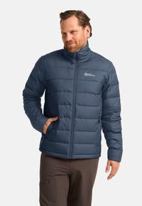 Blaue isolierte Jacke mit Reißverschluss vorne, horizontaler Steppung, hohem Kragen und Logo auf der Brust. Hergestellt aus leichtem, glattem Stoff.