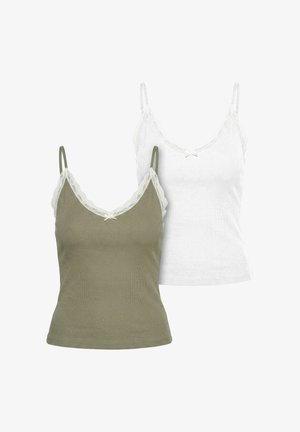 Femeie purtând o jachetă supradimensionată neagră din piele, o camisola verde măsliniu și pantaloni largi din satin, cu sandale negre și ochelari de soare, stând în interior.