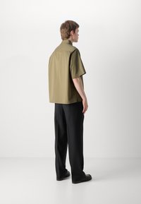 Short-sleeve olive green shirt with a straight cut, side slits, and a classic collar, paired with black wide-leg trousers and loafers.
