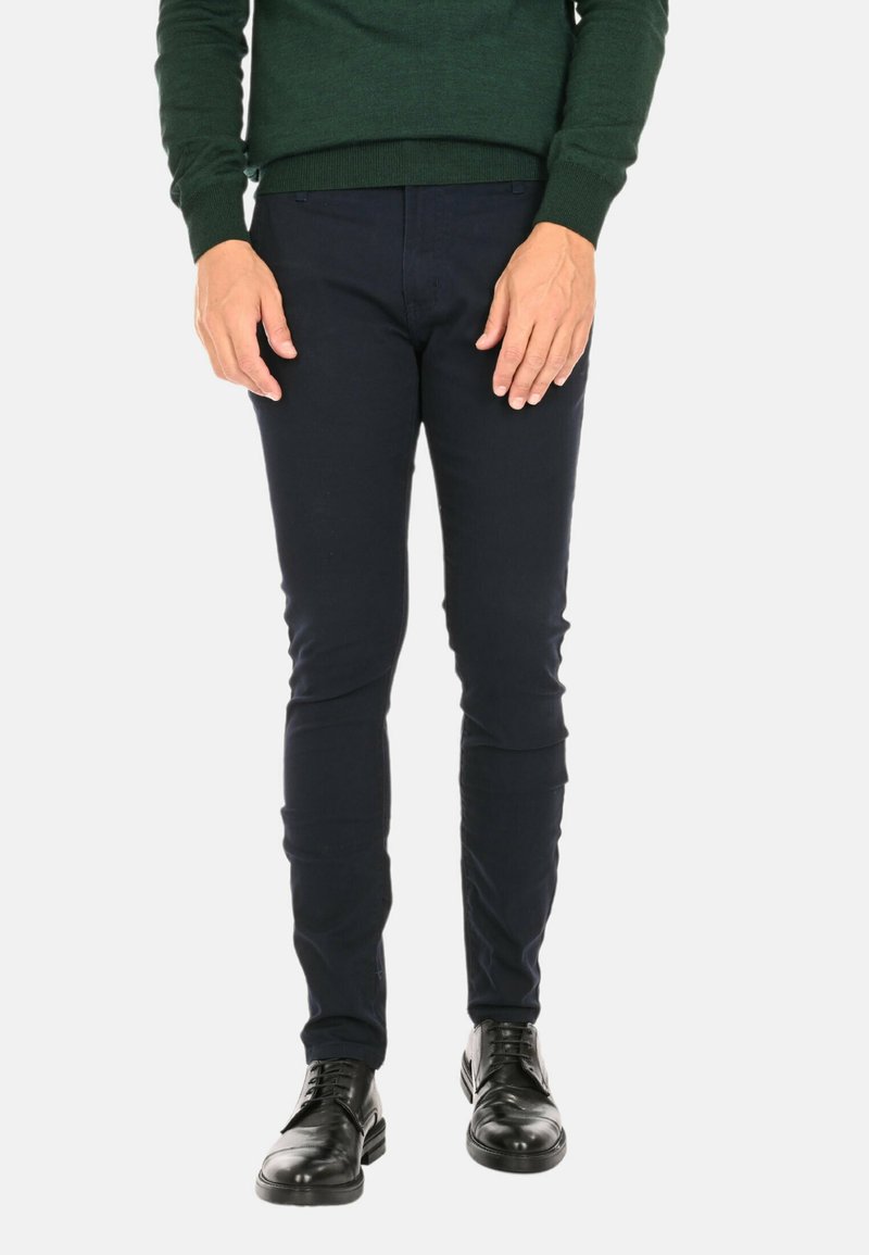 Pantaloni slim fit blu navy in cotone, abbinati a scarpe nere in pelle, caratterizzati da una texture liscia e senza pattern visibili.