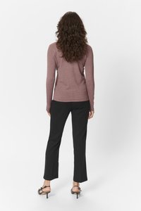 Langarmige, aansluitende top in mauve, gecombineerd met zwarte, rechte broeken en zwarte haksandalen. Het model staat met de rug naar de camera.