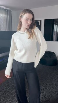 Λευκός πλεκτός πουλόβερ με ριγωτή υφή και μακριά μανίκια, συνδυασμένο με μαύρο, φαρδύ παντελόνι. Το υλικό φαίνεται απαλό, με υφή φινιρίσματος.