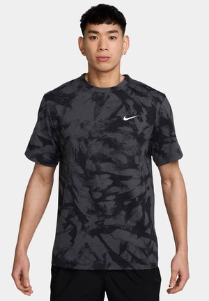 T-shirt de sport noir à manches courtes avec des motifs abstraits gris, col rond et un logo Nike blanc sur la poitrine. Texture de tissu lisse.
