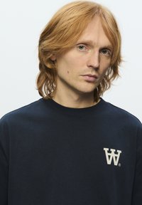 Marineblå bomulds sweatshirt har en rund hals og et lyst logo på venstre bryst. Stoffet har en glat, ensartet tekstur.
