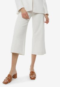 Pantalones anchos recortados blancos con una textura suave, combinados con mule de tacón bloque abierto marrón que cuenta con un acento de cadena.