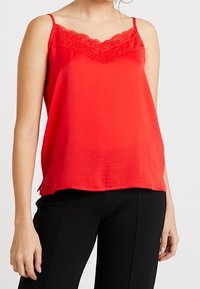 Camisola in raso rosso con un bordo in pizzo floreale lungo il collo e sottili spalline regolabili, dal taglio morbido e texture liscia.