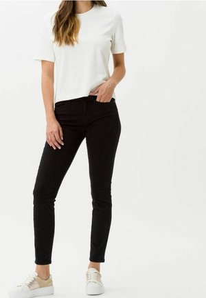 T-shirt blanche à manches courtes associé avec un jean slim noir et des baskets beiges. La tenue présente un design simple et épuré sans motifs.