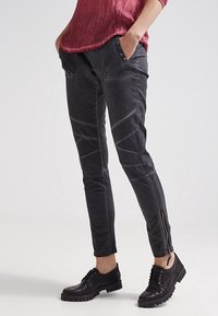 Donkergrijze skinny broek met contrasterende stiksels, zijzakken en ritsen bij de enkels. Gemaakt van duurzame stof met een gladde textuur.