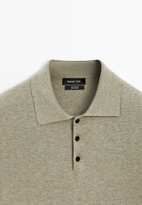 Lichtgrijze katoenen poloshirt met een kraag en drie zwarte knopen van Massimo Dutti, plat gelegd op een witte achtergrond.