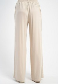Beżowe spodnie szerokie z elastycznym paskiem w talii, gładką teksturą i bocznymi rozcięciami, zaprojektowane z myślą o komforcie i swobodzie ruchów.