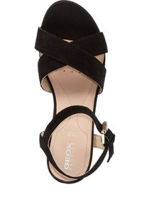 Sandal in suede nera con fasce incrociate e punta chiusa. Presenta una soletta beige e una fascia laterale con un accentuato fibbia metallica.